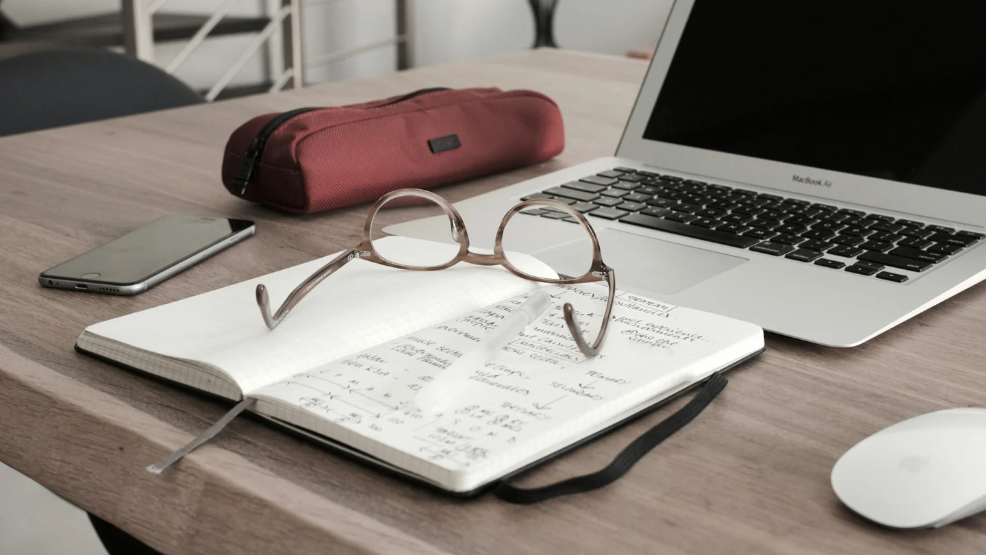 Research notes and glasses beside a laptop