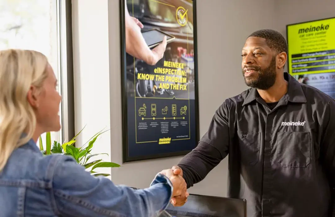 A Meineke service advisor greeting a customer at the service counter.